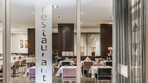 Interior de restaurante con mesas y sillas, un separador de vidrio con la palabra 'restaurant' y una decoración moderna.