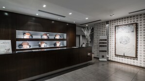 Un área de recepción con un mostrador de madera oscura, estantes con objetos decorativos y una obra de arte enmarcada de gran tamaño en la pared.