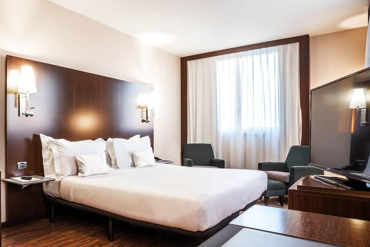 Ein Hotelzimmer mit einem großen Bett, zwei Sesseln, einem Schreibtisch und einem Fernseher.