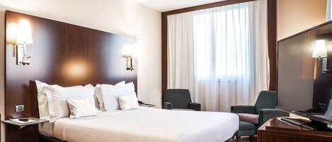 Une chambre d’hôtel avec un grand lit, deux fauteuils, un bureau et une télévision.