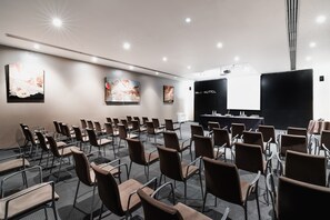 A conference room with rows of chairs, a stage with a black backdrop, and artwork on the walls. - Max Hotel Livorno (Livorno)