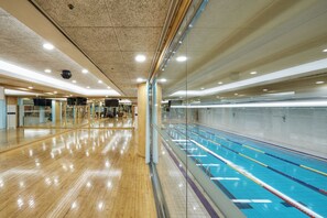 An indoor swimming pool with clear lane markings, a wooden floor, and a glass wall on one side.