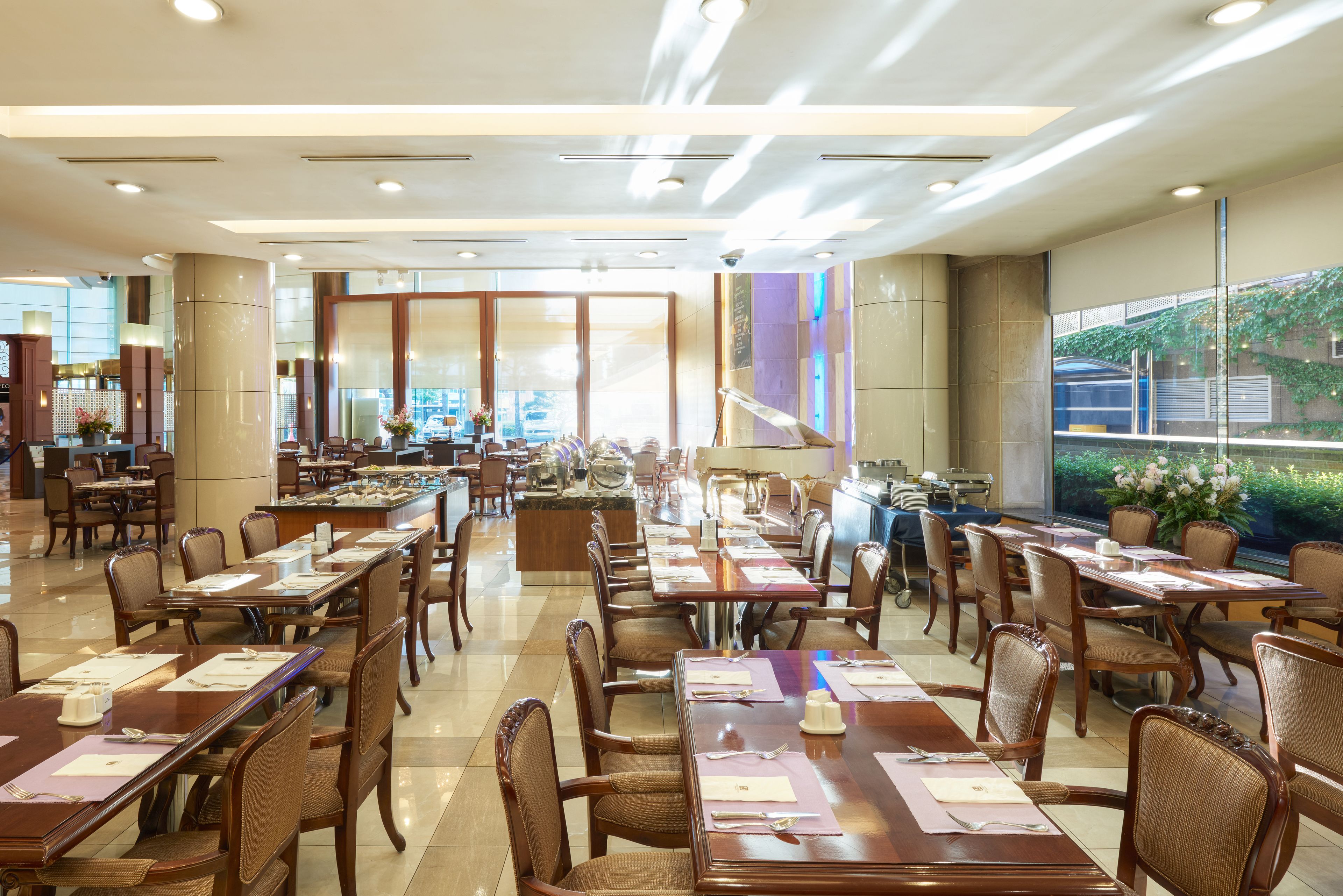 A spacious dining area with multiple tables and chairs, large windows, and a modern ceiling design.