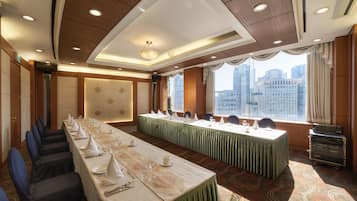 Une salle de conférence avec une longue table préparée pour une réunion, une vue sur la ville à travers de grandes fenêtres et un plafond doté d’un éclairage encastré.