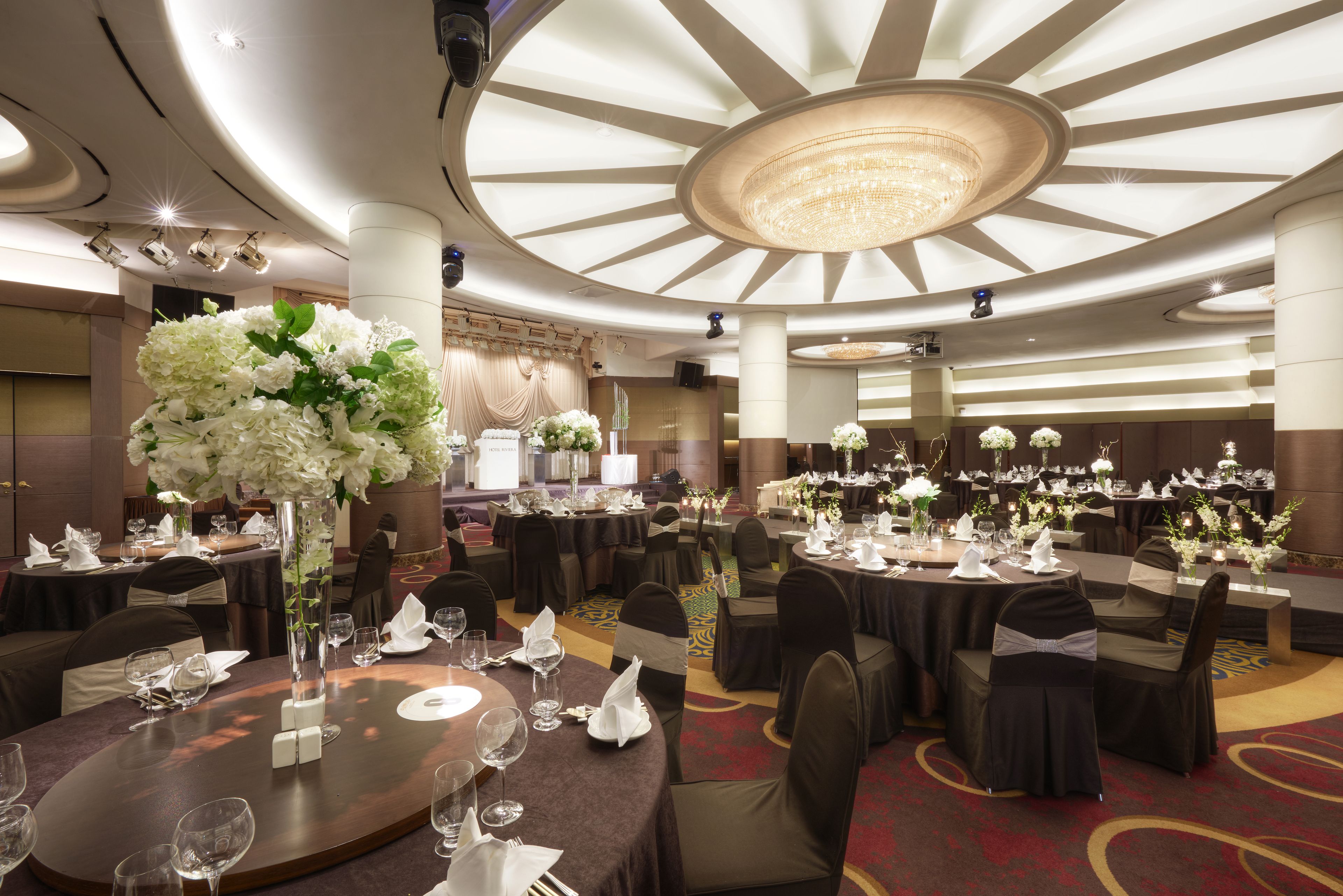 Un salón de banquetes con mesas redondas, sillas y centros de mesa florales.