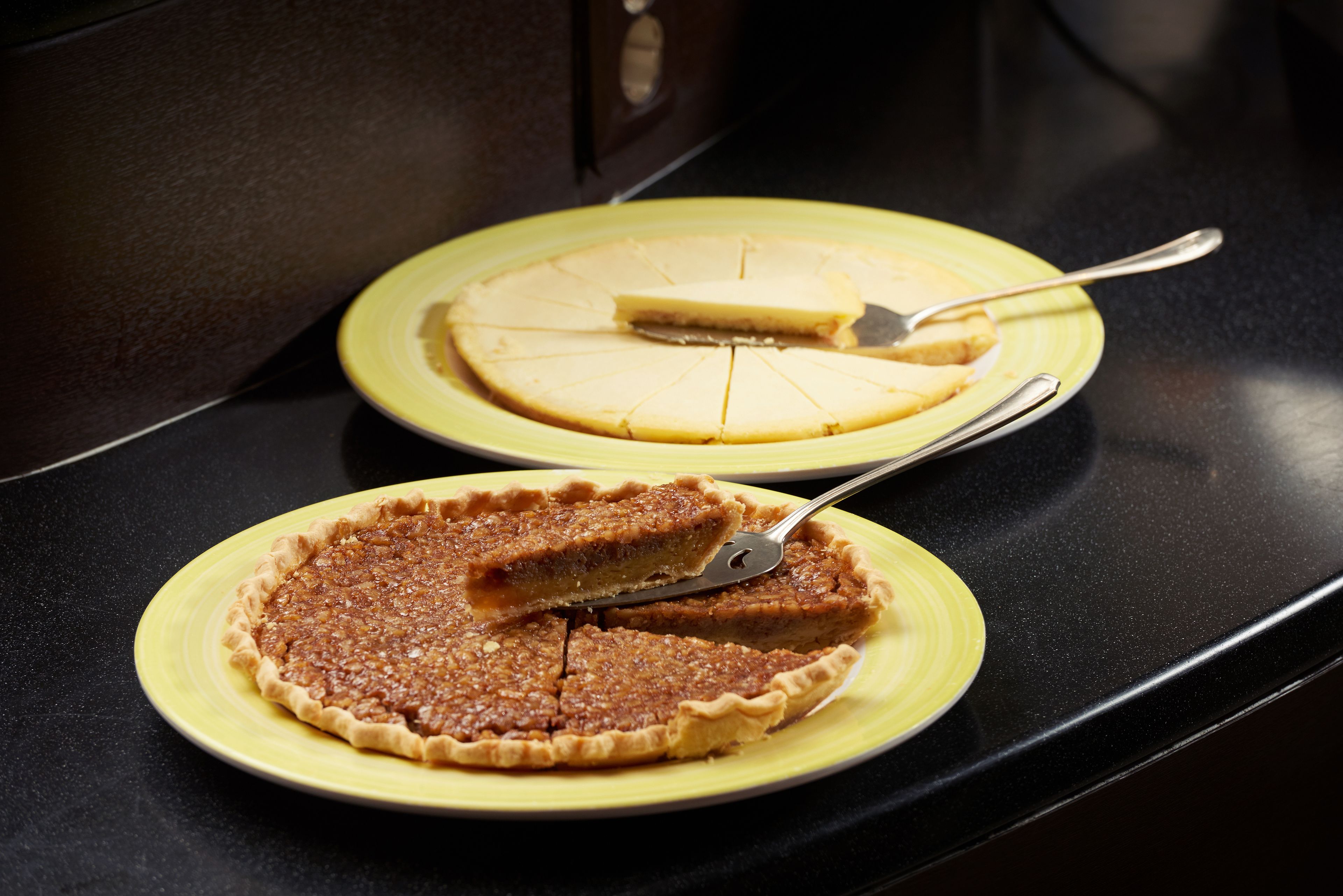 Two pies on yellow plates on a black countertop.
