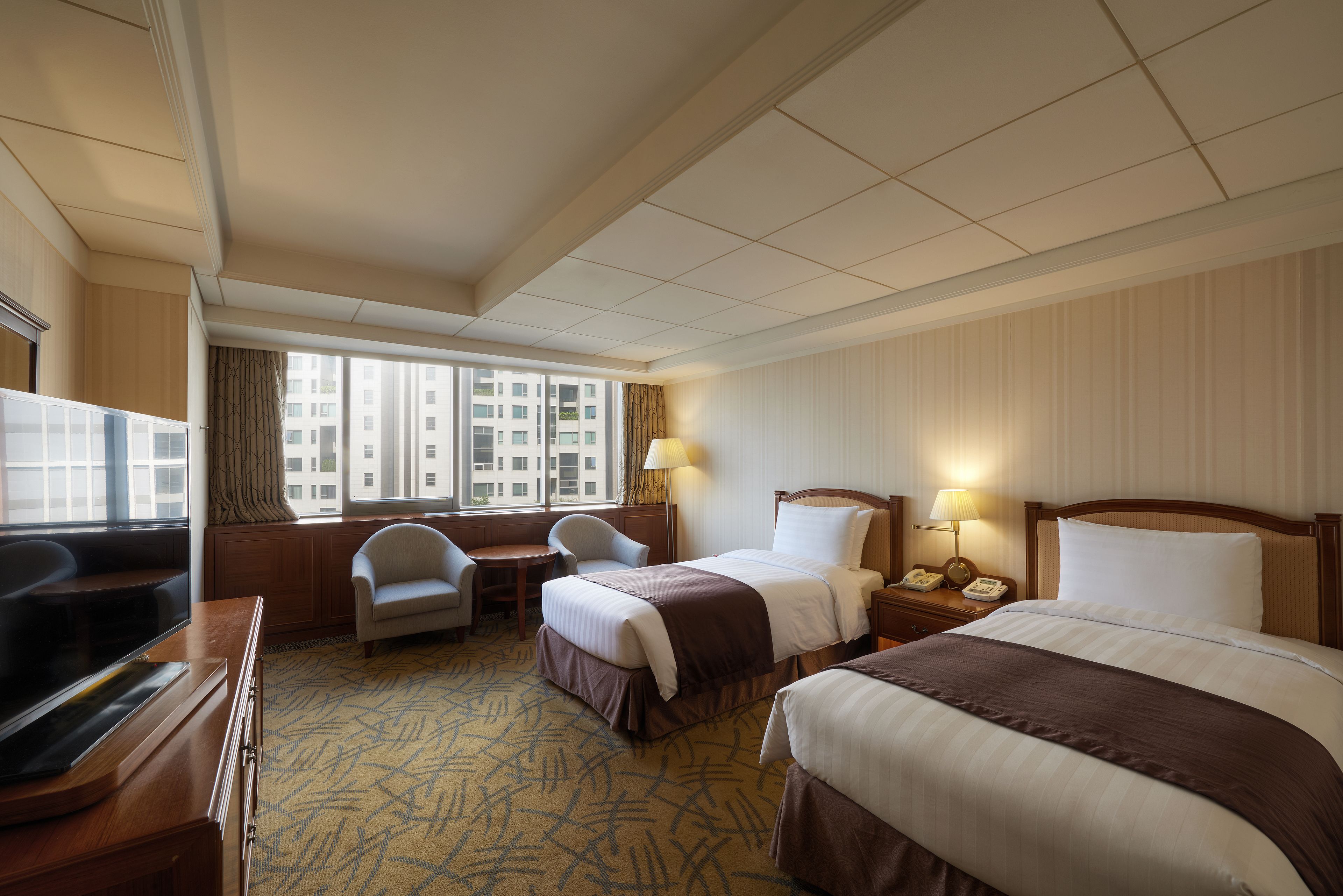 Ein Hotelzimmer mit zwei Betten, einem Schreibtisch, einem Sessel und einem Fernseher.