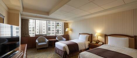 A hotel room with two beds, a desk, a chair, and a TV.