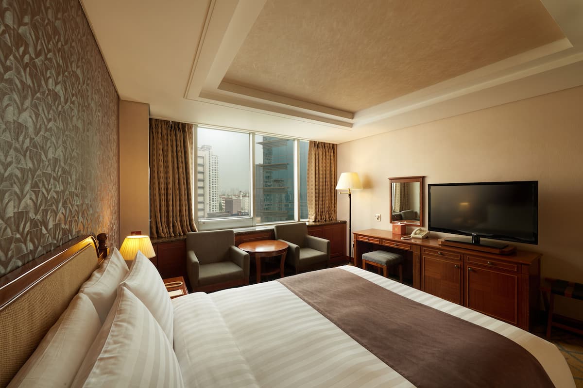 A hotel room with a large bed, a desk with a flat-screen TV, a small table, and two chairs.