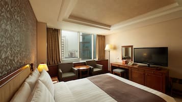 A hotel room with a large bed, a desk with a flat-screen TV, a small table, and two chairs.