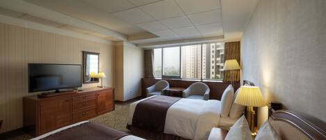 A hotel room with two beds, a TV, a desk, and a window with a city view.