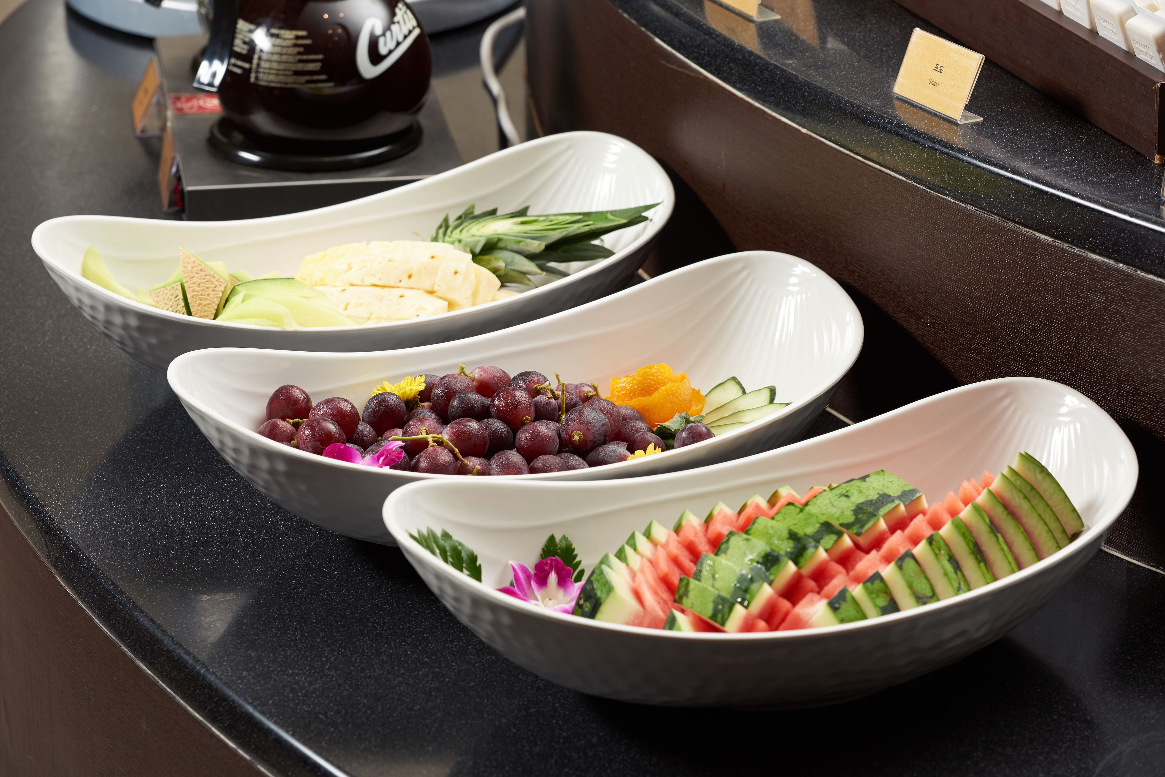 Three white bowls with various fruits and vegetables on a black countertop.
