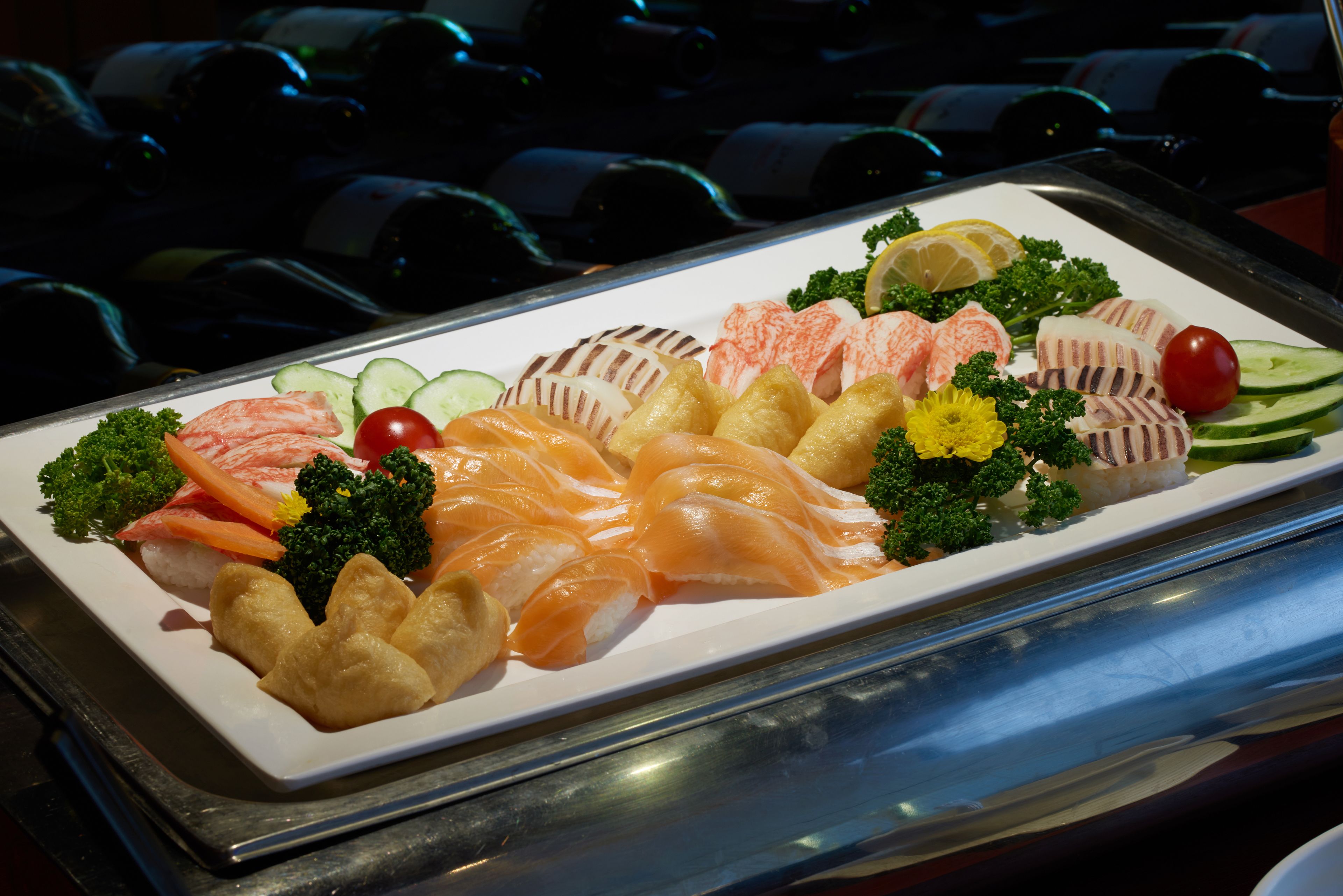 Una bandeja de sushi y sashimi sobre un plato blanco, adornada con vegetales y rodajas de limón.