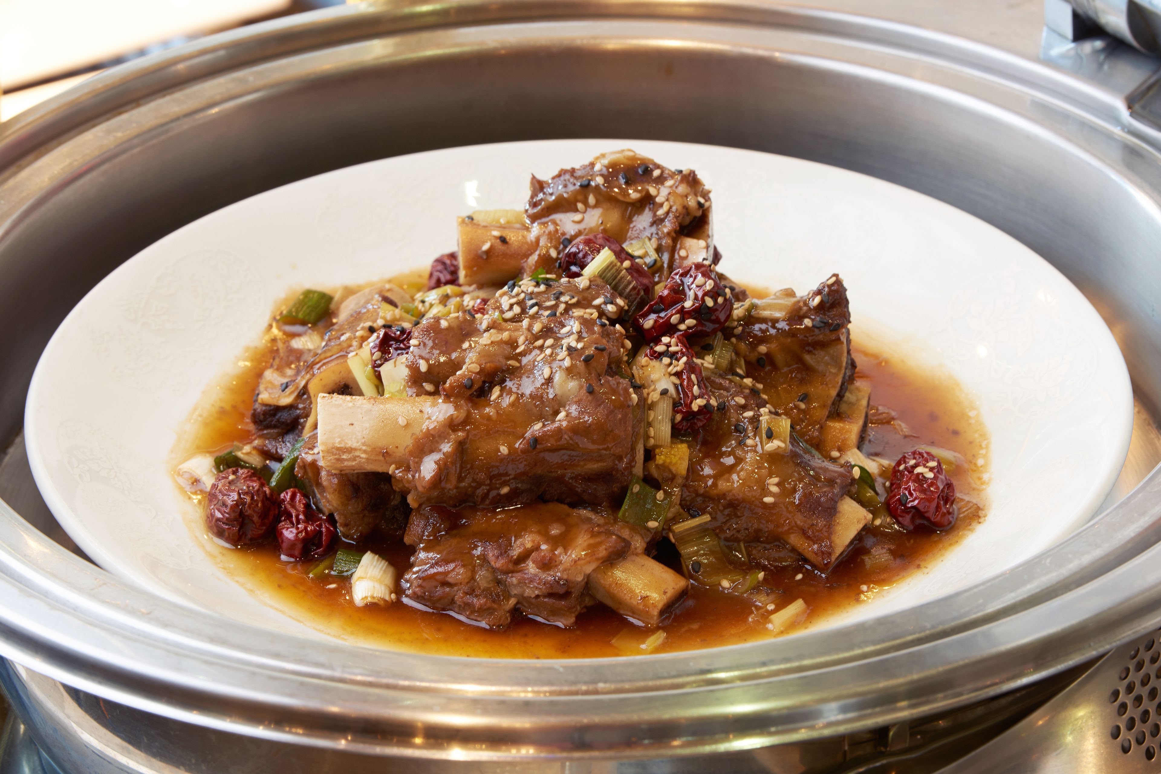 Un plato de panceta de cerdo estofada con vegetales y semillas de sésamo.