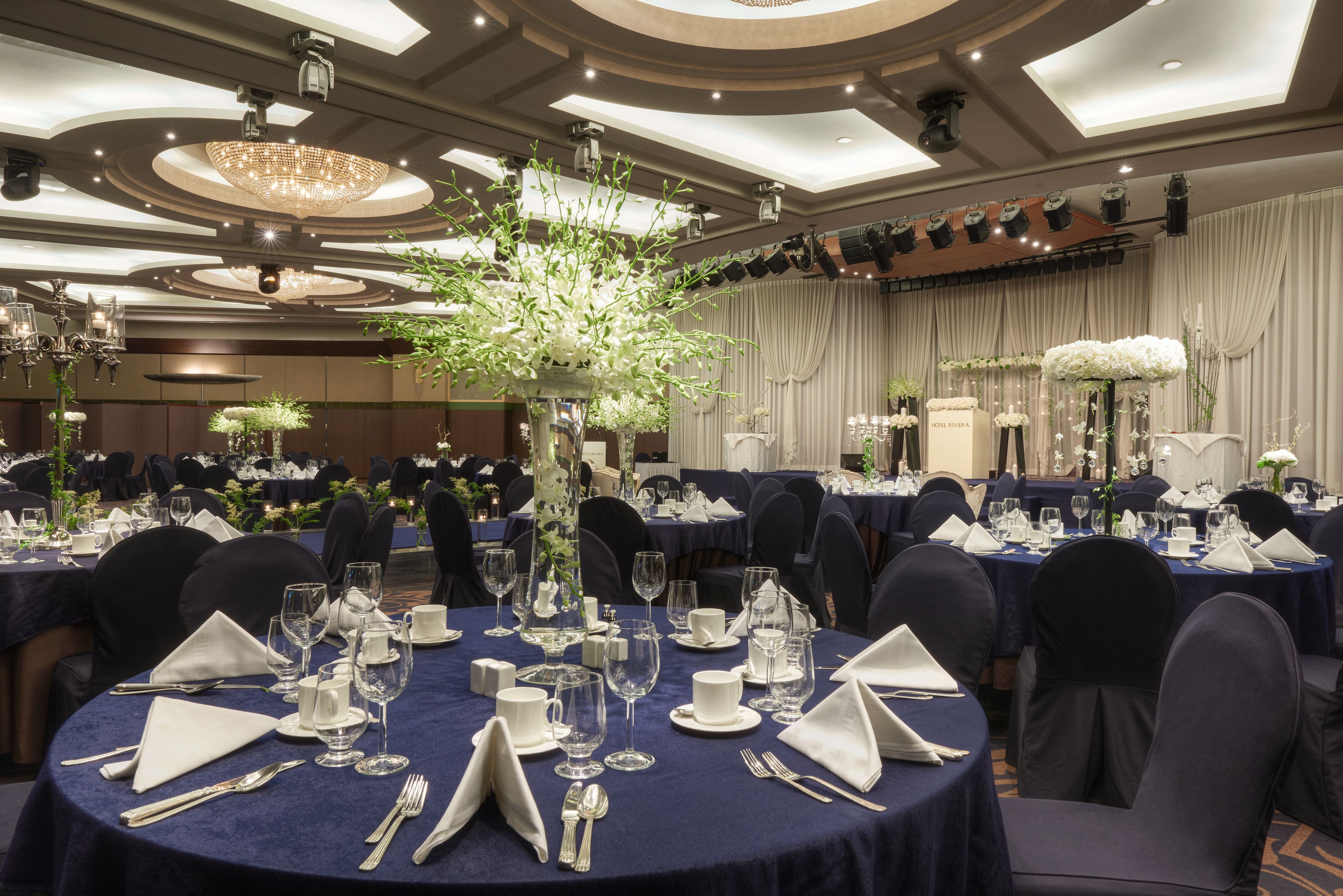 Un salón de banquetes con mesas redondas dispuestas para un evento formal, con elegantes mantelería y un gran centro de flores.