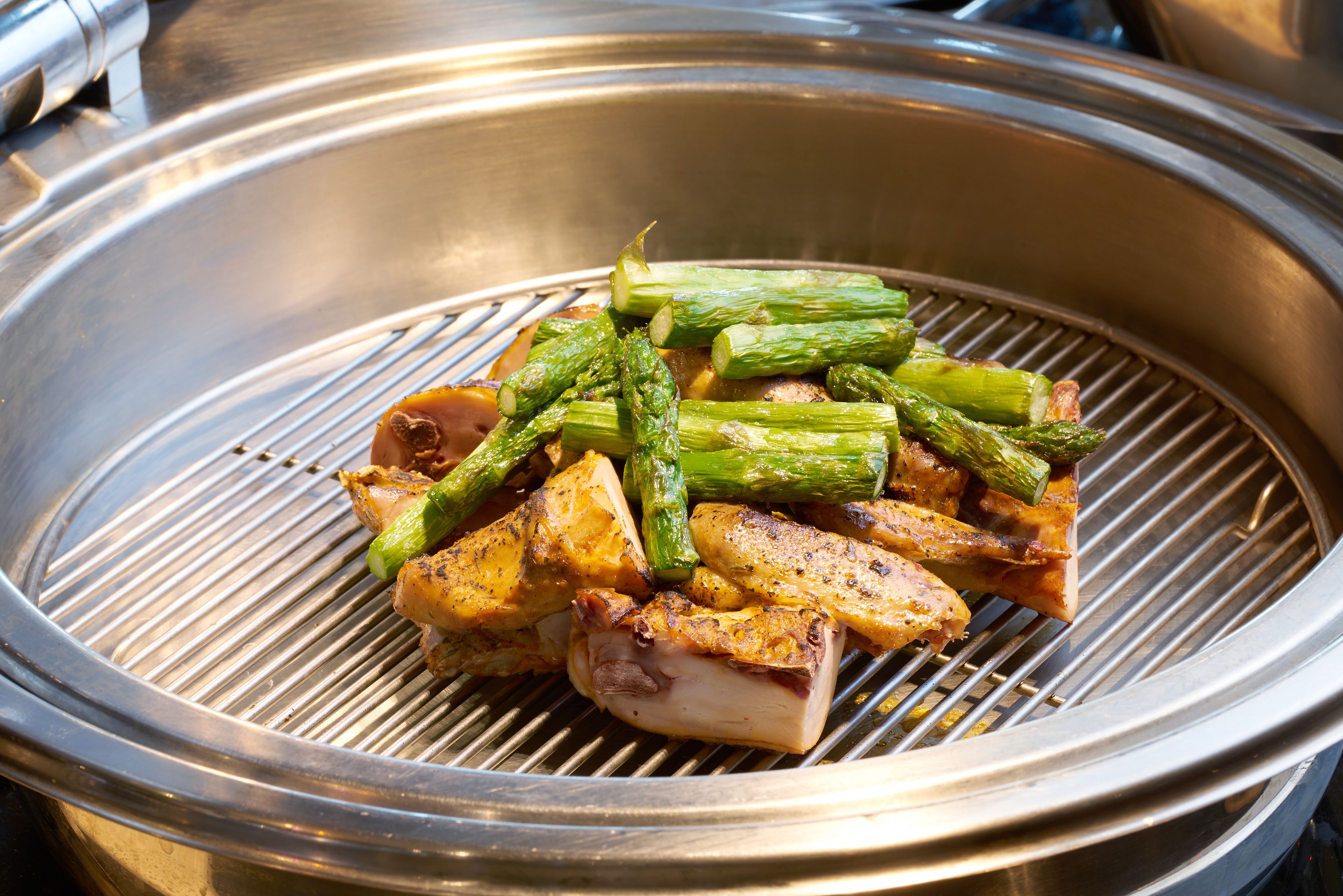 A stainless steel grill with food items including asparagus and meat.