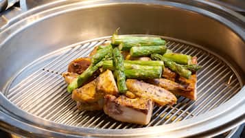 A stainless steel grill with food items including asparagus and meat.