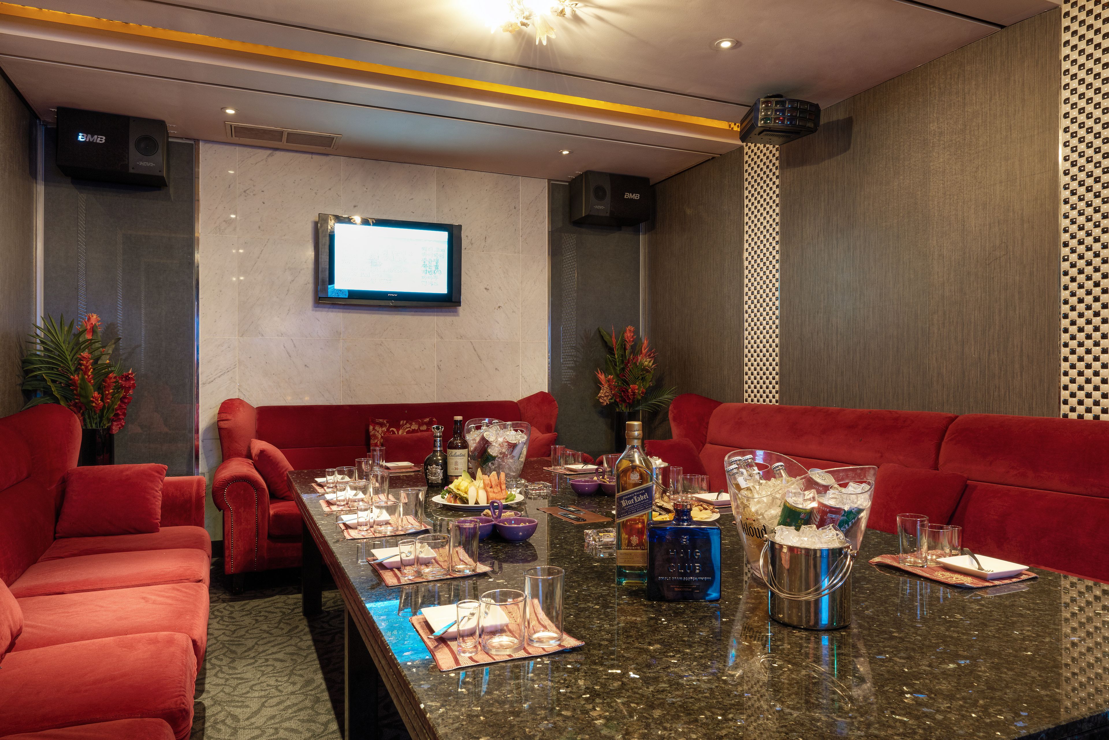 A conference room with a long table set for a meeting, red sofas, a projector screen, and a speaker system.