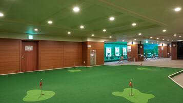 Habitación con paneles de madera, alfombra verde con marcadores de hoyos de golf y zona de recepción con fondo verde y asientos.