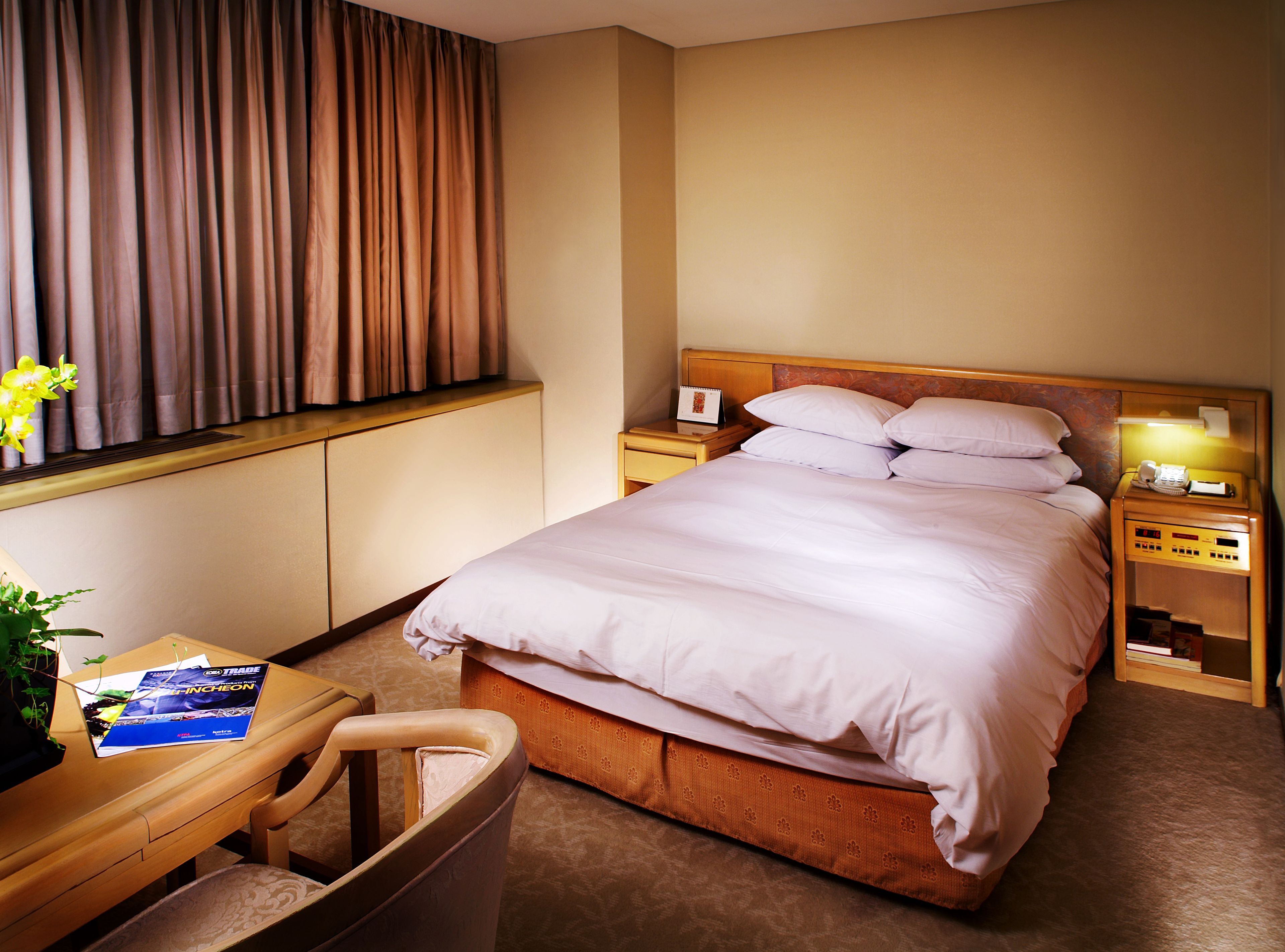 Habitación de hotel con cama, mesitas de noche, escritorio con silla y ventana con cortinas.