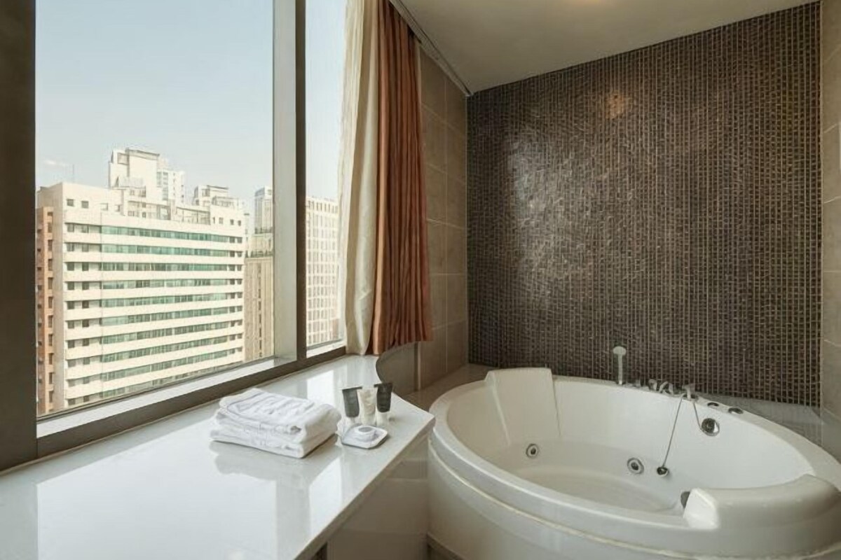 Een moderne badkamer met een groot bad, een raam met gordijnen en uitzicht op gebouwen.
