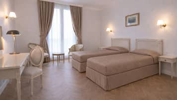 A hotel room with two beds, a desk, a chair, a small table, and two wall-mounted lamps.