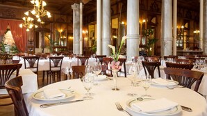 A formal dining room with round tables, white tablecloths, and elegant chairs. - Grand Hotel Moderne (Lourdes)