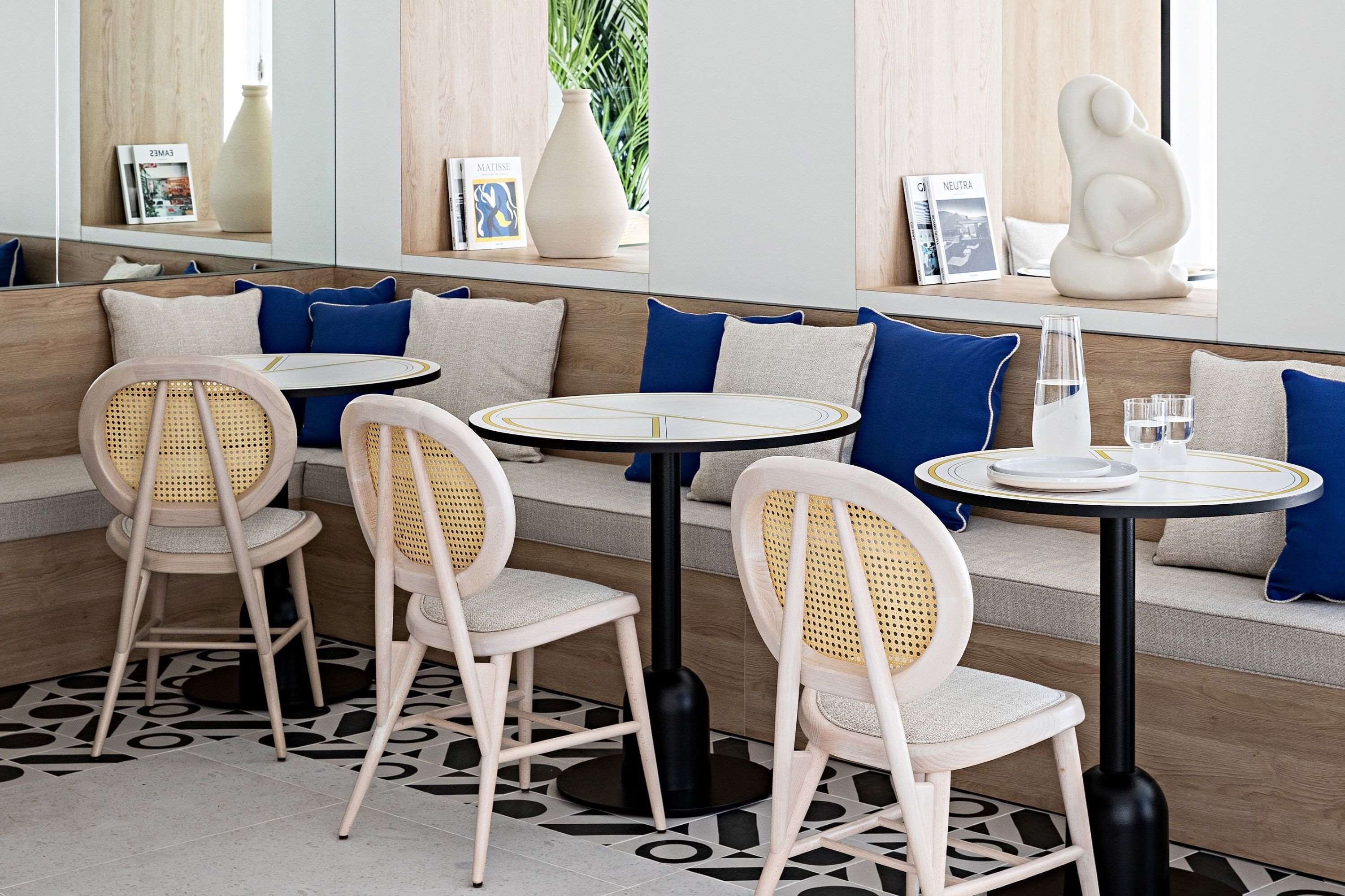 Um restaurante moderno com cadeiras de vime, mesas redondas e um banco de madeira com almofadas azuis.