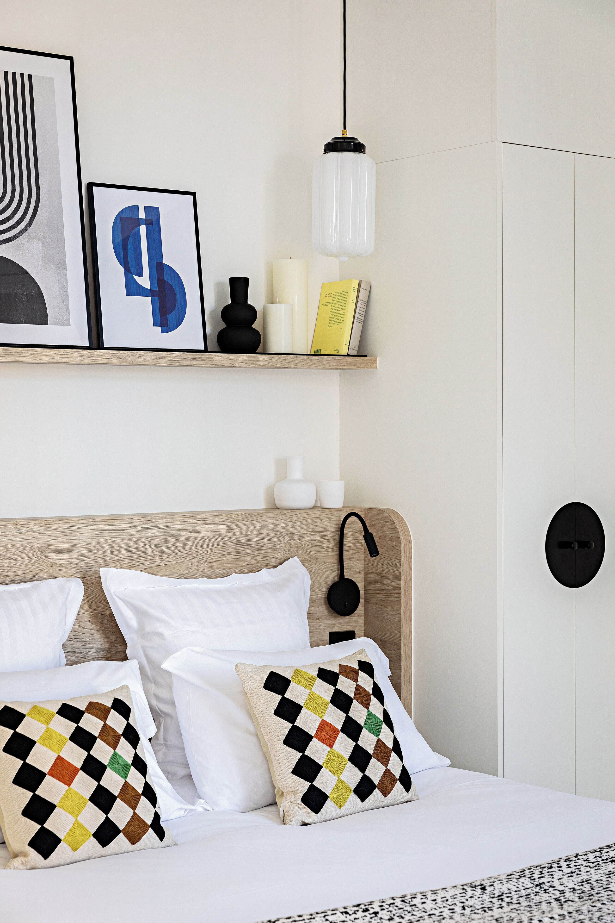 Une chambre à coucher bien rangée, avec une tête de lit en bois, du linge de lit blanc et des coussins décoratifs.