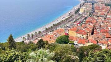 Un paisaje urbano costero con playa, zona densamente poblada y un puente de piedra con gente.