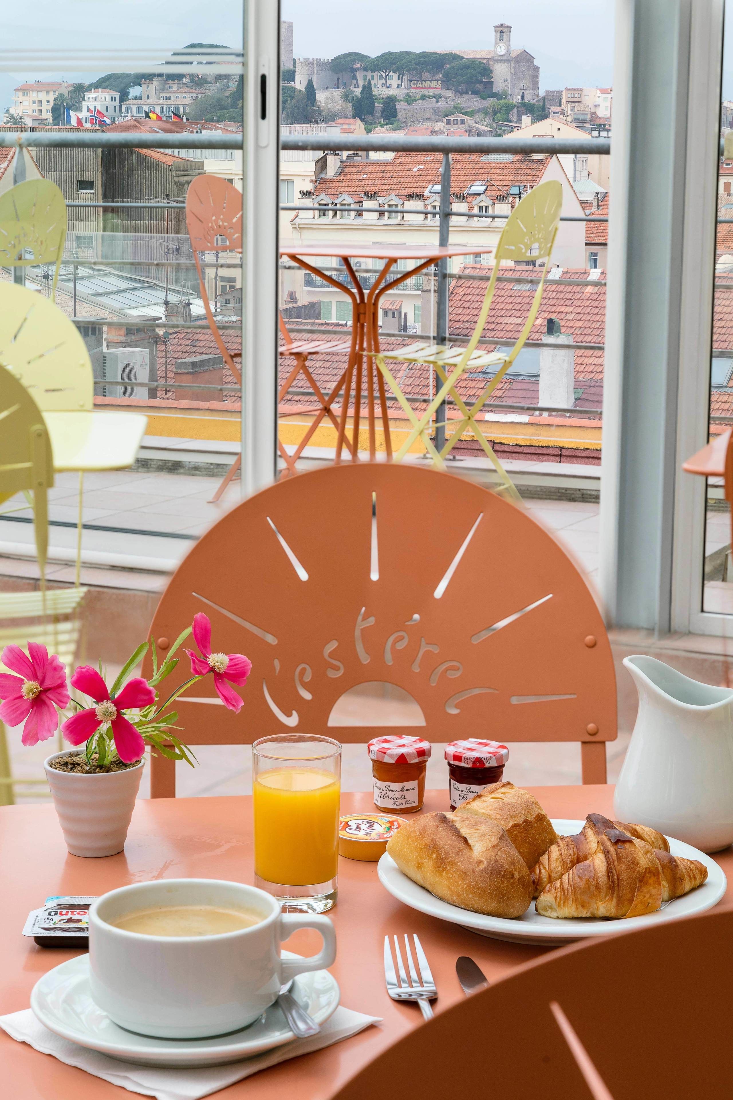A breakfast table with a cup of coffee, croissants, and a glass of orange juice.