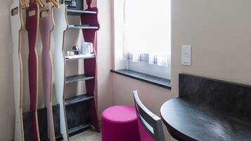 Une pièce comprenant une table à manger, une chaise rose, un pouf rose, une armoire avec un miroir et une fenêtre avec des rideaux.