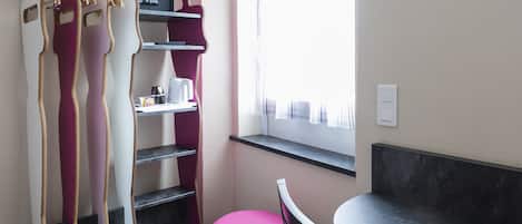 A room with a dining table, a pink chair, a pink ottoman, a wardrobe with a mirror, and a window with curtains.
