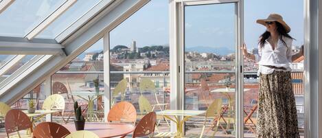 A balcony with a glass roof, outdoor seating, and a city view.