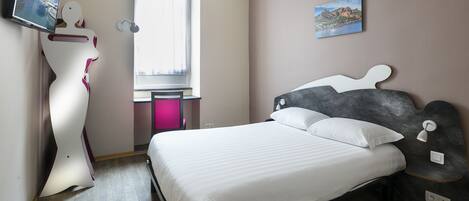 Un dormitorio con cama, televisor montado en la pared, escritorio y ventana.