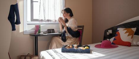 A hotel room with a bed, a table with a tray of food, a window with curtains, and a chair.
