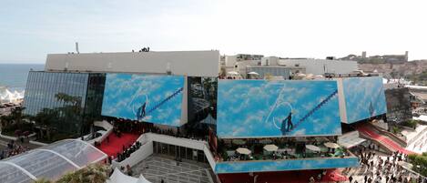 A modern building with a glass facade, outdoor seating area, and a red carpet event.