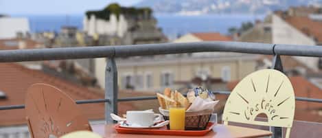 Un balcon avec une table préparée pour le petit-déjeuner, comprenant du pain, une tasse et un verre de jus d’orange.