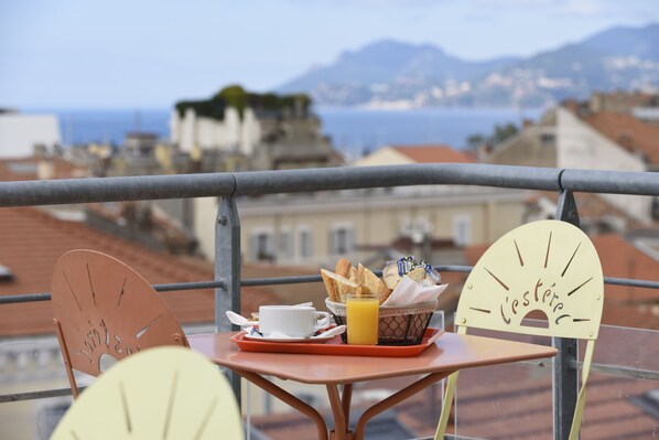 A balcony with a table set for breakfast, including bread, a cup, and a glass of orange juice.