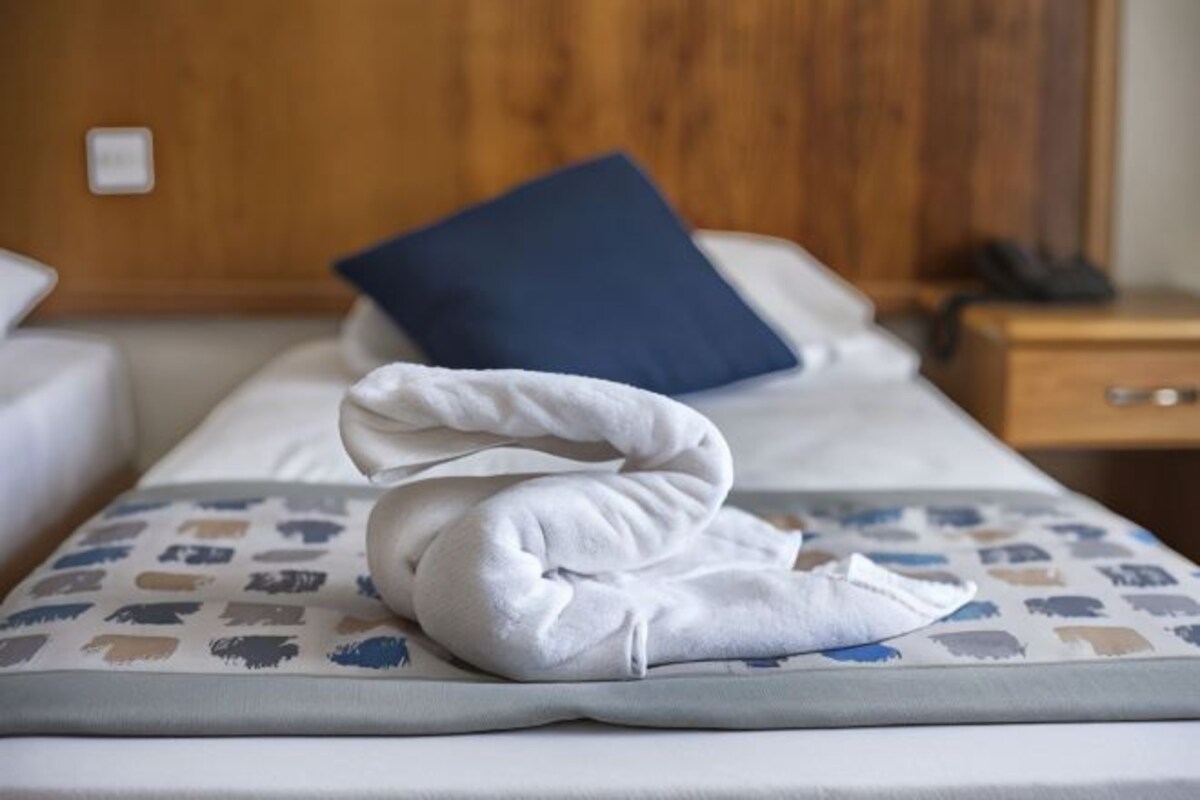 A neatly made bed with a blue pillow and a white towel folded on a patterned bedspread.