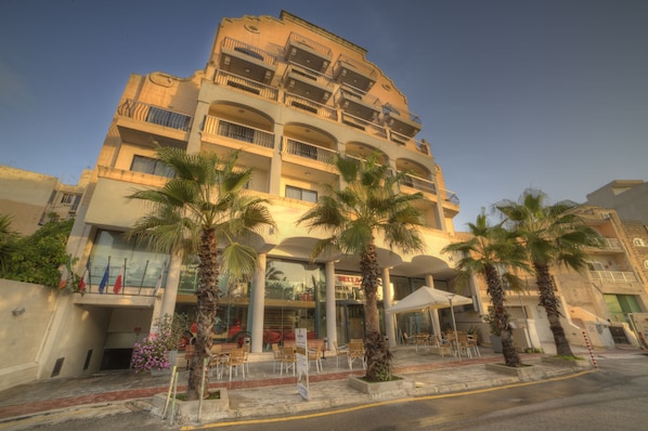 Un hotel de varios pisos con balcones, palmeras y mobiliario exterior.