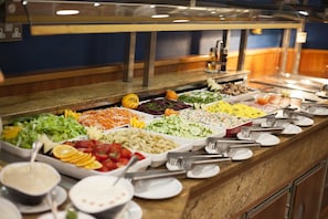 Un bufé con diversas opciones de comida, como ensaladas, frutas y pasta.