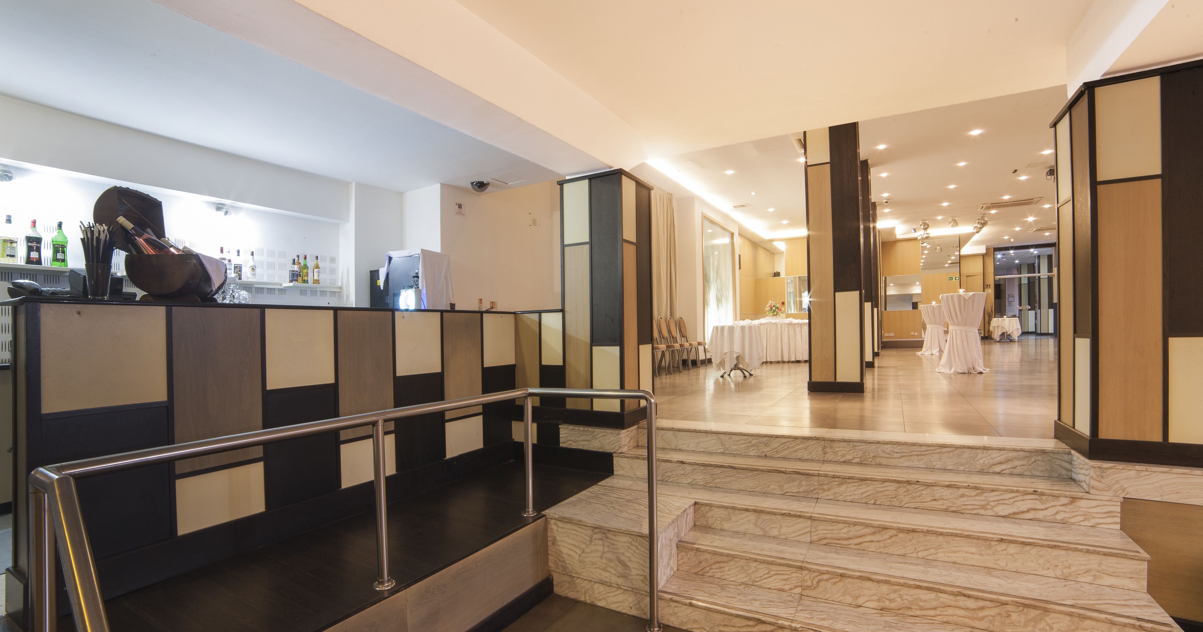 Rebedor d'hotel amb una escala de marbre, una zona de recepció amb mostrador i una sala de menjador amb taules preparades per a un àpat.