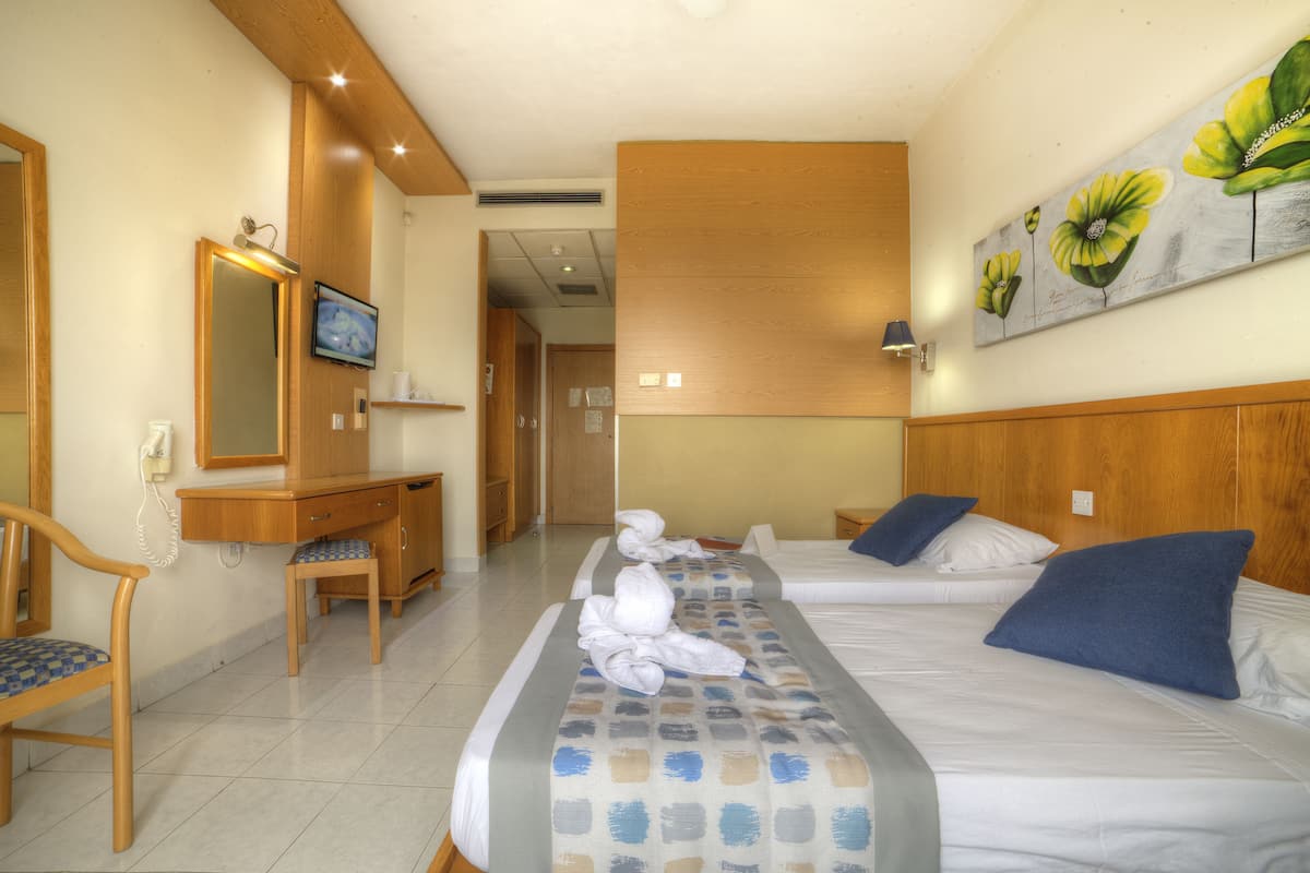 Una habitació d'hotel amb dos llits, un escriptori, una cadira i un quadre a la paret.