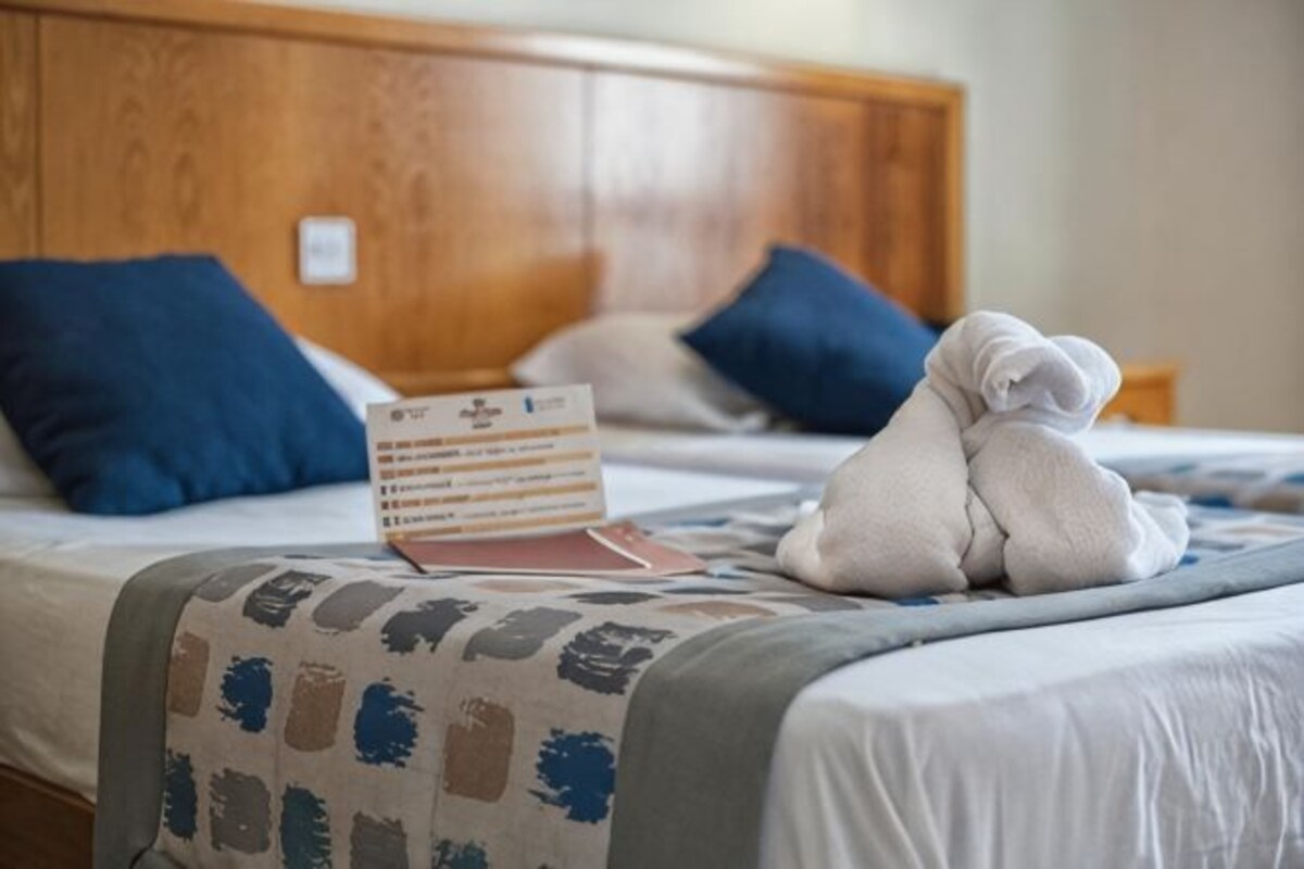 A neatly made bed with a wooden headboard, a stack of brochures, and a pair of folded towels.