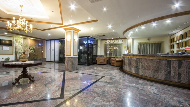 A hotel lobby with a marble floor, a reception desk, a chandelier, and a large mirror. - Canifor Hotel (St. Paul's Bay)