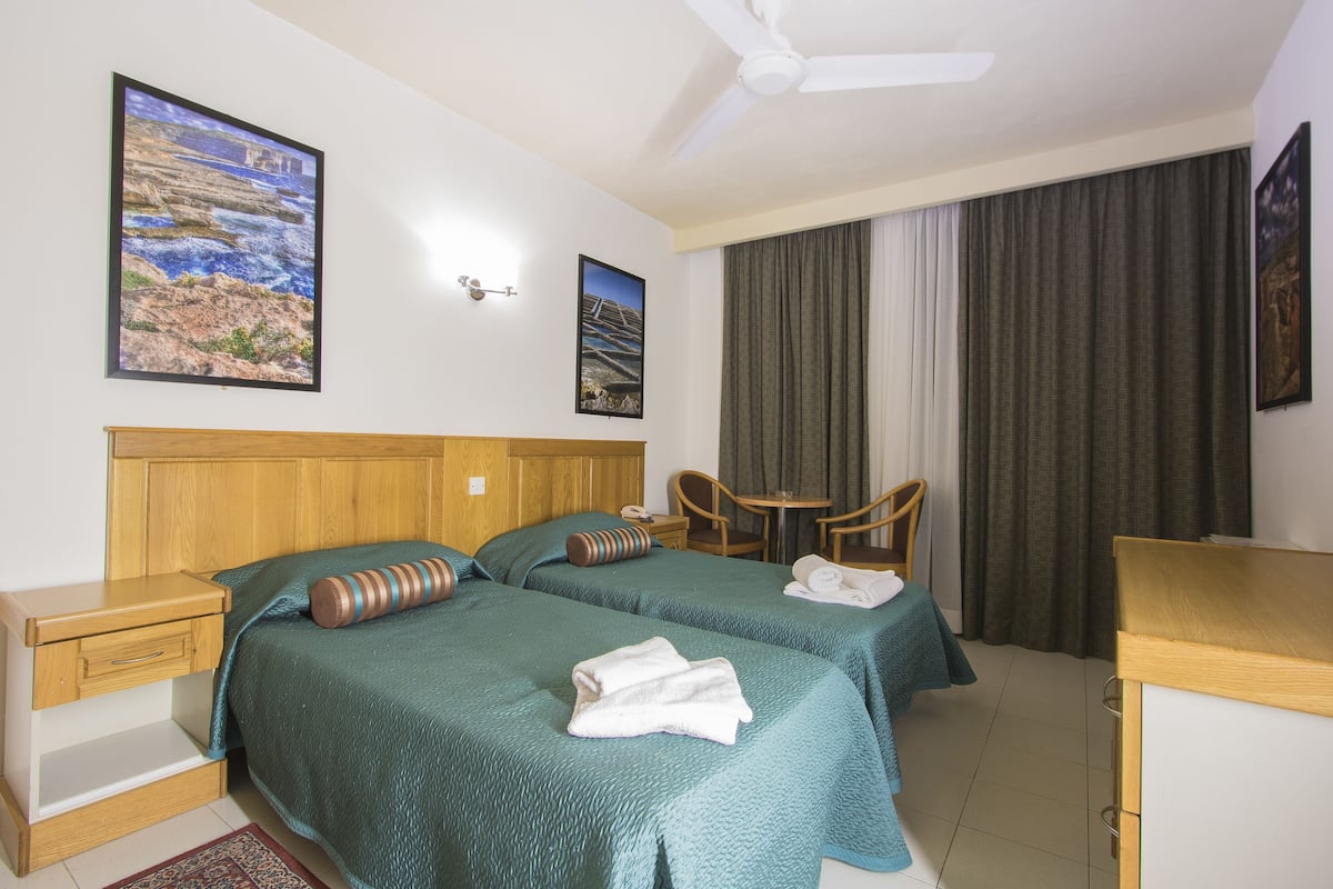 Habitación de hotel con dos camas, un escritorio, una silla, una mesa y un ventilador de techo.