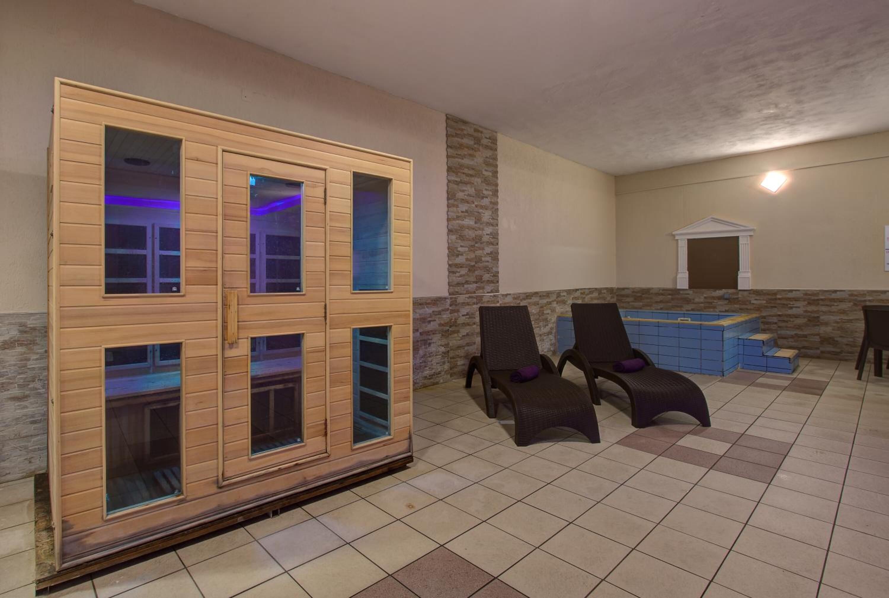 Un'area benessere con armadietti in legno, due poltrone reclinabili, una vasca idromassaggio blu e un muro in pietra.