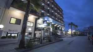 A multi-story hotel with balconies, a covered outdoor seating area, and a palm tree in the foreground. - Canifor Hotel (St. Paul's Bay)