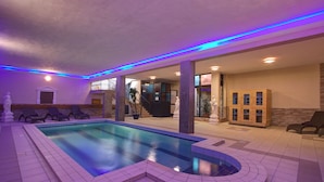 An indoor swimming pool with a curved edge, surrounded by lounge chairs and a staircase leading to an upper level. - Canifor Hotel (St. Paul's Bay)